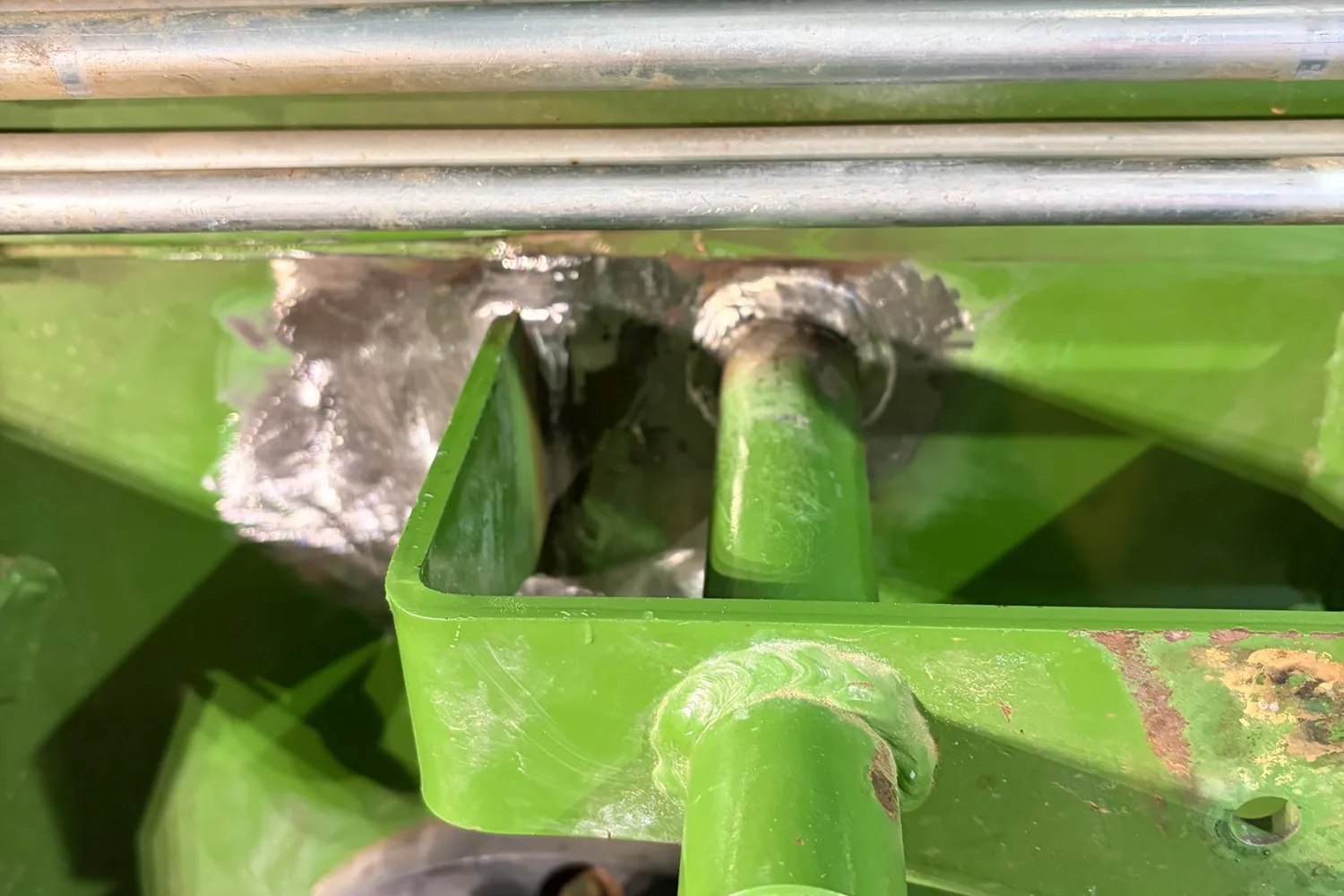 Hay baler crack repair near Prairie: finished MIG welds beside the bracket and around the pin, in bare metal before painting