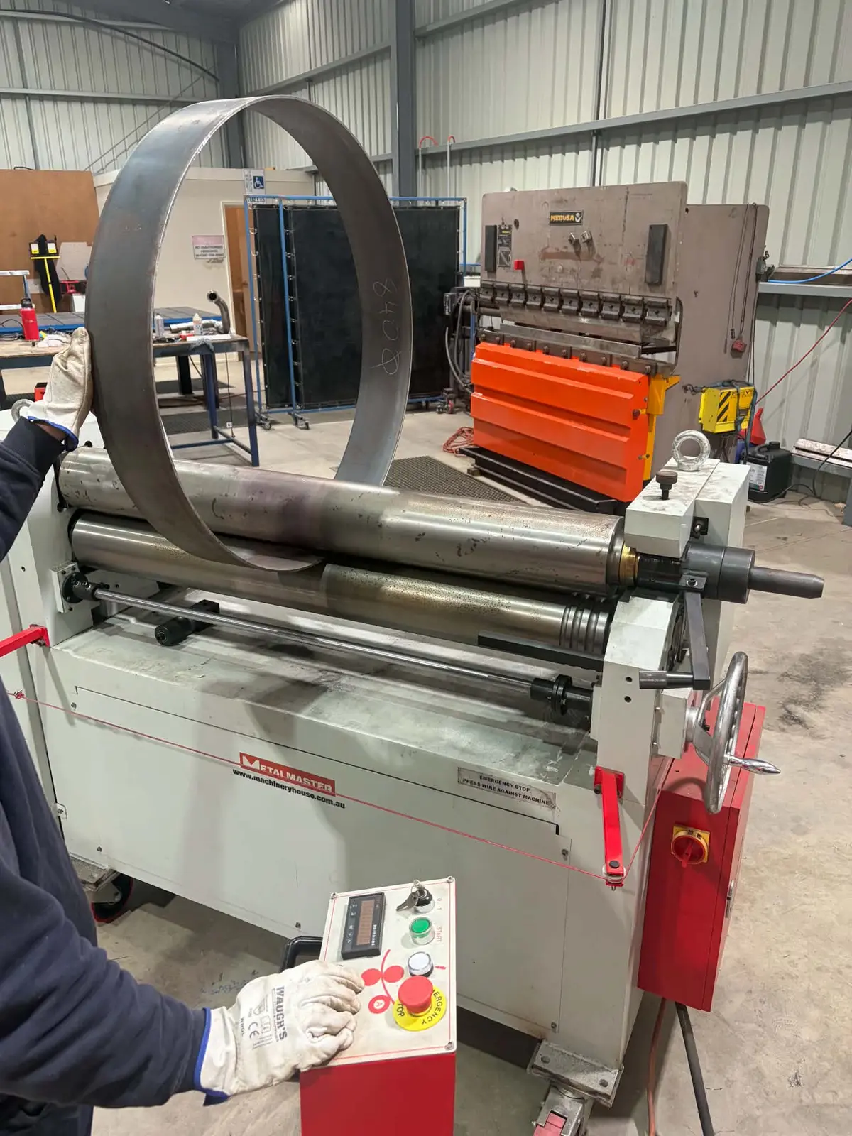 Troy operating the plate roller in the MMW workshop, with the press brake behind